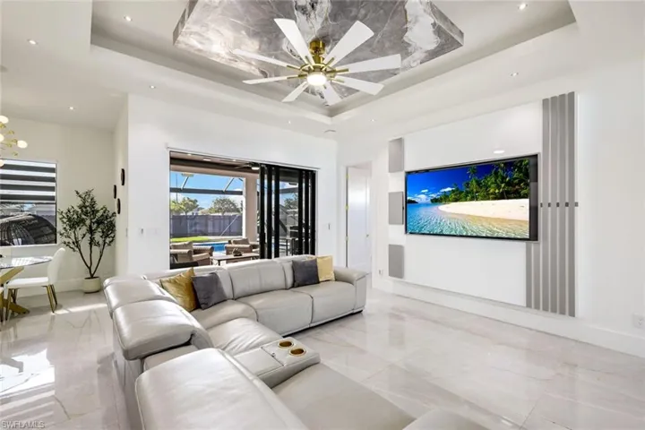 Living room featuring a tray ceiling, ceiling fan with notable chandelier, marble finish floor, and baseboards