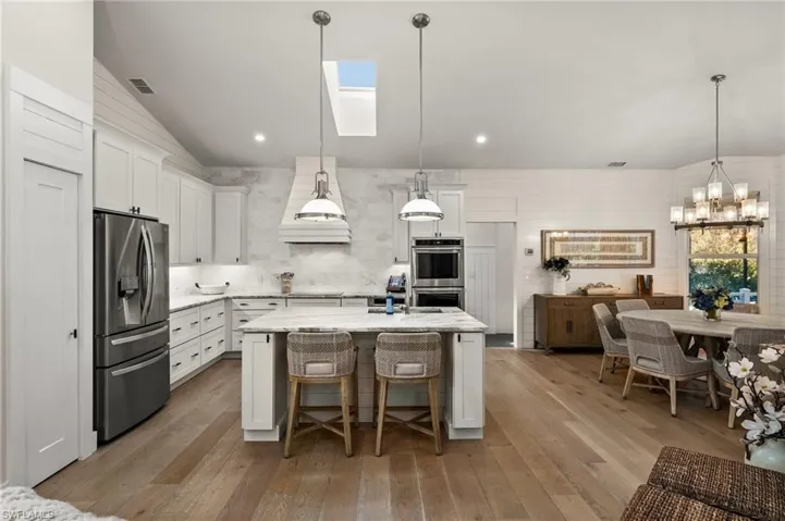 Kitchen featuring vaulted ceiling with skylight, decorative light fixtures, white cabinetry, and stainless steel appliances