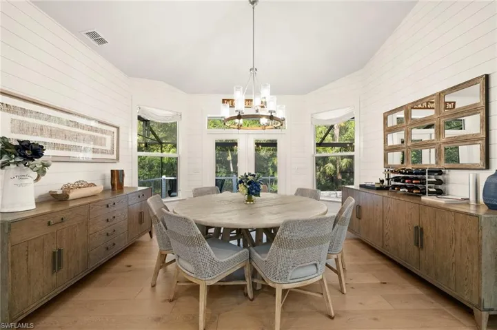Dining area featuring french doors, light wood-type flooring, brick wall, a chandelier, and lofted ceiling