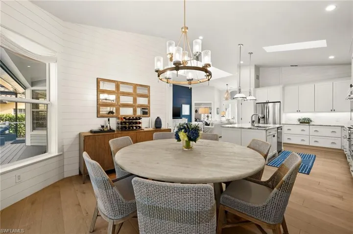 Dining room featuring wood walls, high vaulted ceiling, an inviting chandelier, light hardwood / wood-style flooring, and a skylight