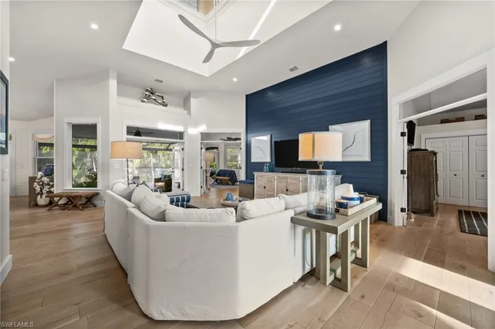 Living room featuring ceiling fan, light hardwood / wood-style flooring, high vaulted ceiling, and wooden walls