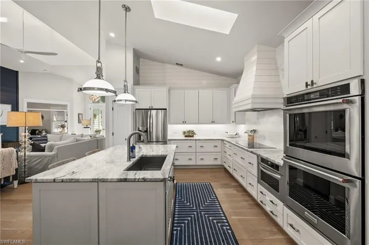 Kitchen featuring custom exhaust hood, white cabinets, a center island with sink, sink, and appliances with stainless steel finishes
