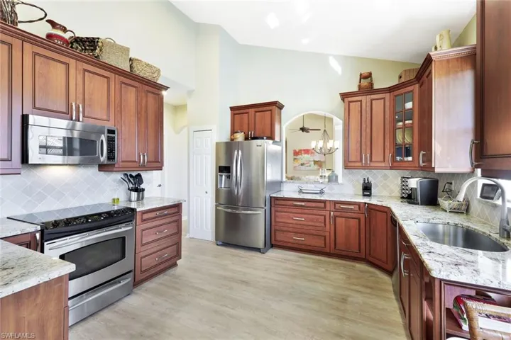 Kitchen with stainless steel appliances, light stone countertops, lofted ceiling, glass insert cabinets, and tasteful backsplash