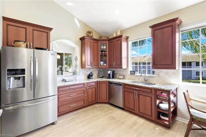 Kitchen with stainless steel appliances, light stone countertops, vaulted ceiling, light wood-style floors, and glass fronted cabinets