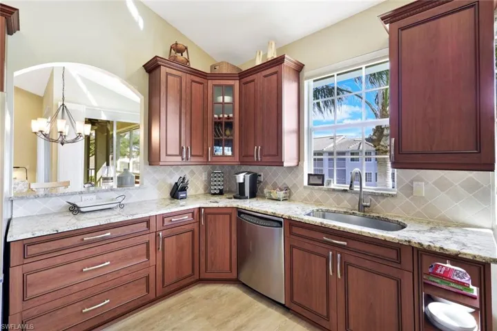 Kitchen with light stone counters, dishwasher, glass fronted cabinets, and light wood-style flooring