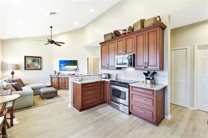 Kitchen with open floor plan, light stone countertops, stainless steel appliances, a peninsula, and light wood-style flooring