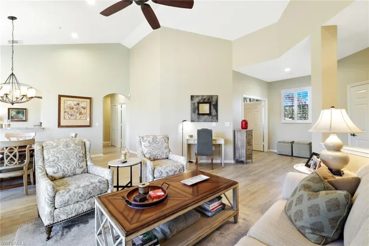Living room featuring light wood-style floors, hanging lights, arched walkways, a ceiling fan, and vaulted ceiling
