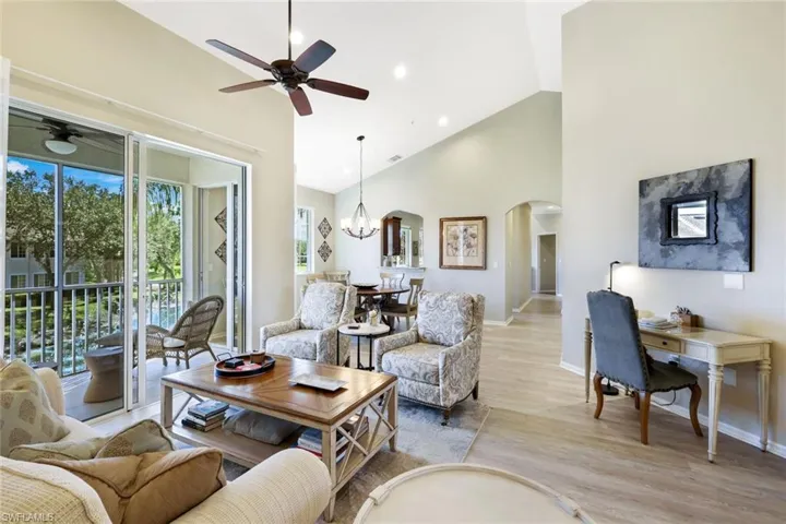 Living area with ceiling fan, suspended lighting, light wood-style flooring, lofted ceiling, and arched walkways