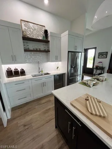 Kitchen featuring dark cabinets, light stone counters, backsplash, open shelves, and refrigerator