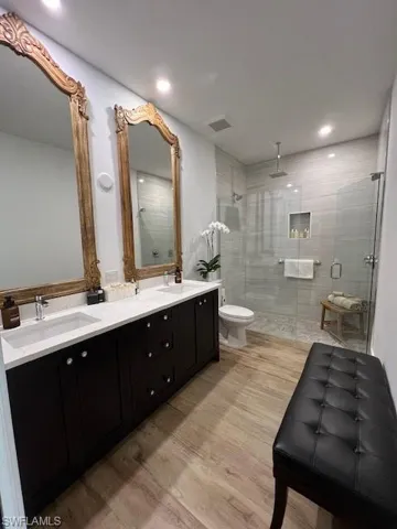 Full bath featuring a shower stall, double vanity, light wood finished floors, and recessed lighting