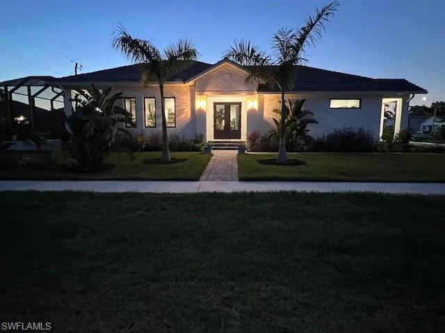 Ranch-style house featuring a front lawn, stucco siding, and french doors
