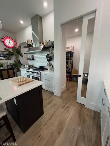 Kitchen featuring light stone countertops, decorative backsplash, light wood-style floors, exhaust hood, and stove