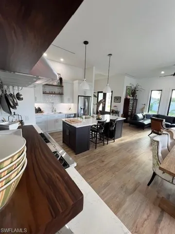 Kitchen featuring pendant lighting, white cabinetry, light wood-type flooring, extractor fan, and light stone countertops
