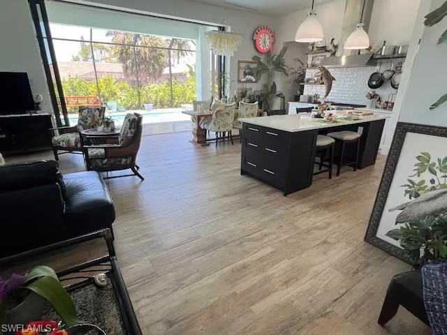 Kitchen featuring dark cabinets, pendant lighting, a breakfast bar area, light wood-style flooring, and a center island with sink
