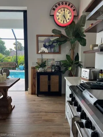 Kitchen view of range, white cabinets, light wood-style flooring, and a sunroom