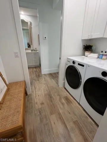 Washroom with light wood-type flooring, washer and dryer, and cabinet space