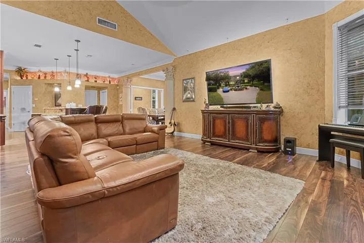 Spacious living area featuring high vaulted ceilings, rich wood-finish flooring, a wall-mounted television, and a built-in media console