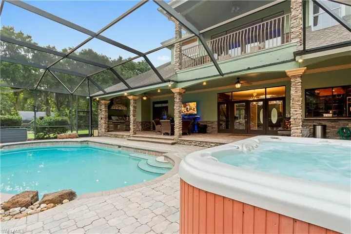 Screened outdoor living area featuring a built-in swimming pool, integrated spa, and an expansive patio paved with interlocking pavers