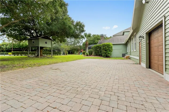 Expansive paver driveway leading to a two-car garage with wood-paneled doors