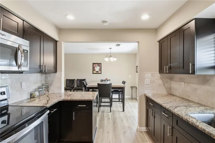 Kitchen featuring backsplash, appliances with stainless steel finishes, light stone countertops, a chandelier, and light wood-style floors