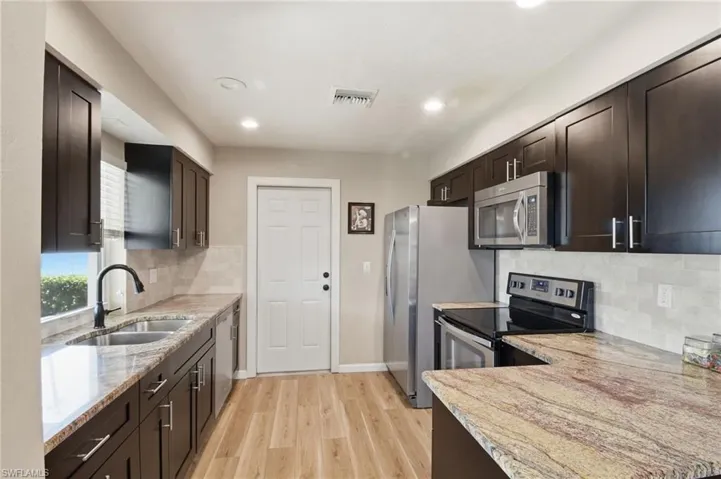 Kitchen featuring dark brown cabinets, appliances with stainless steel finishes, light stone countertops, backsplash, and recessed lighting
