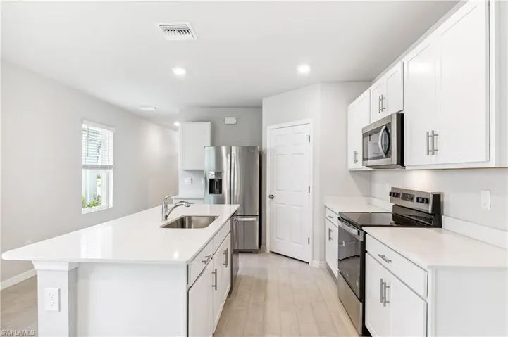 Kitchen featuring stainless steel appliances, light wood-style flooring, light countertops, recessed lighting, and a center island with sink