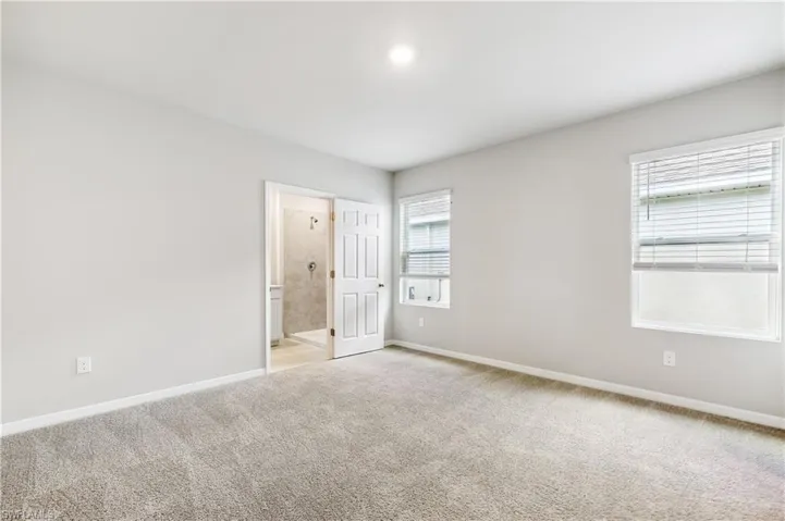 Unfurnished bedroom with light colored carpet, multiple windows, and ensuite bathroom