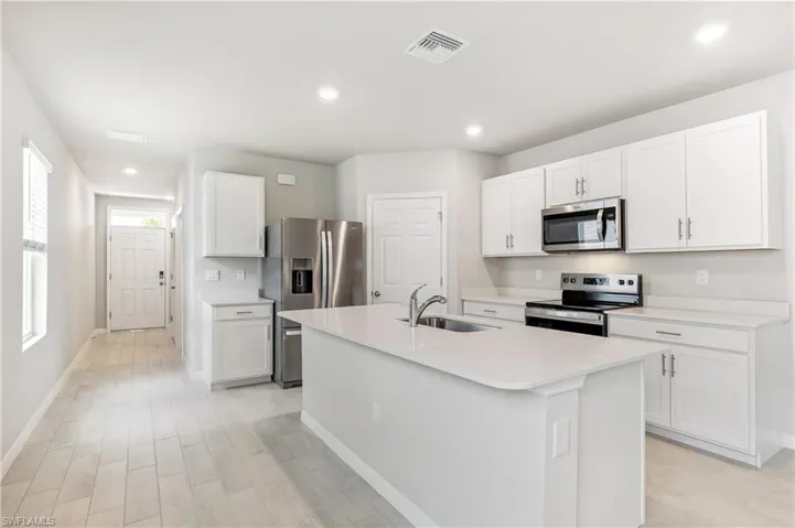Kitchen featuring appliances with stainless steel finishes, light wood-style floors, light countertops, a center island with sink, and white cabinets