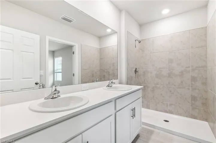 Full bathroom featuring double vanity, a tile shower, tile patterned flooring, and recessed lighting