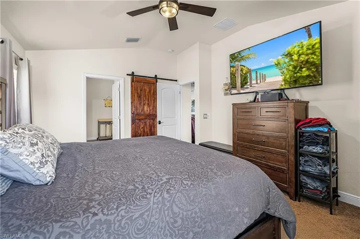 Bedroom with lofted ceiling, light carpet, a ceiling fan, and a barn door
