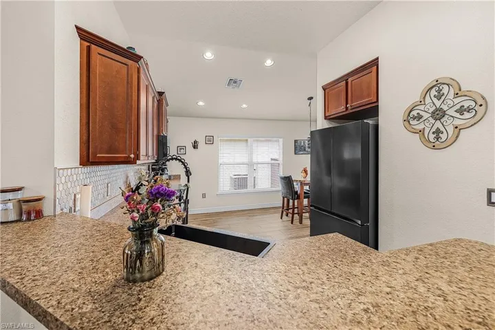 Kitchen with freestanding refrigerator, light stone counters, tasteful backsplash, recessed lighting, and light wood-style floors