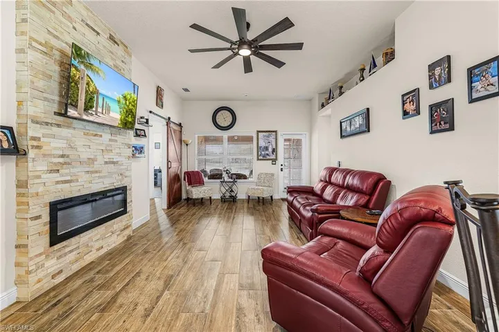 Living room featuring a barn door, ceiling fan, a stone fireplace, and light wood-type flooring