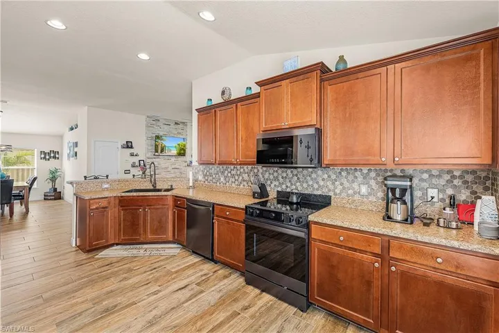 Kitchen featuring black range with electric cooktop, wood finish cabinetry, a peninsula, vaulted ceiling, and stainless steel microwave