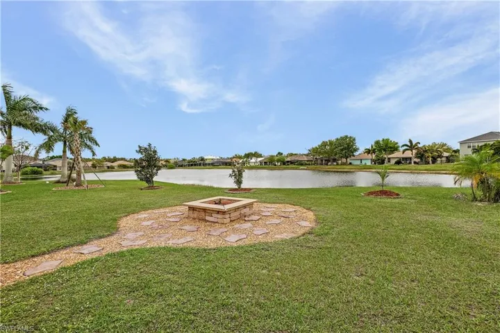 View of grassy yard featuring a fire pit, a water view, a residential view, and a patio area