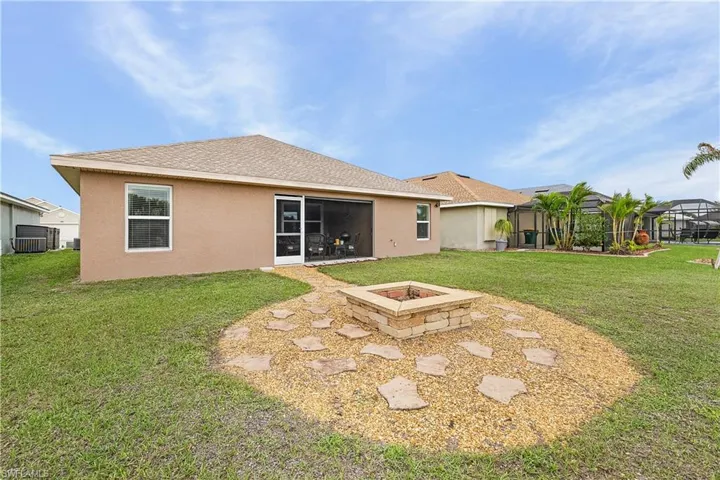 Rear view of property featuring an outdoor fire pit, a shingled roof, stucco siding, a yard, and a sunroom