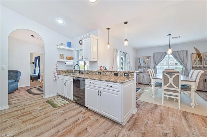 Kitchen with arched walkways, light stone countertops, white cabinetry, and pendant lighting