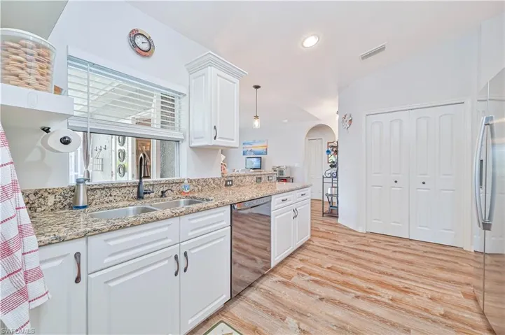 Kitchen with white cabinets, arched walkways, light stone counters, light wood finished floors, and stainless steel appliances