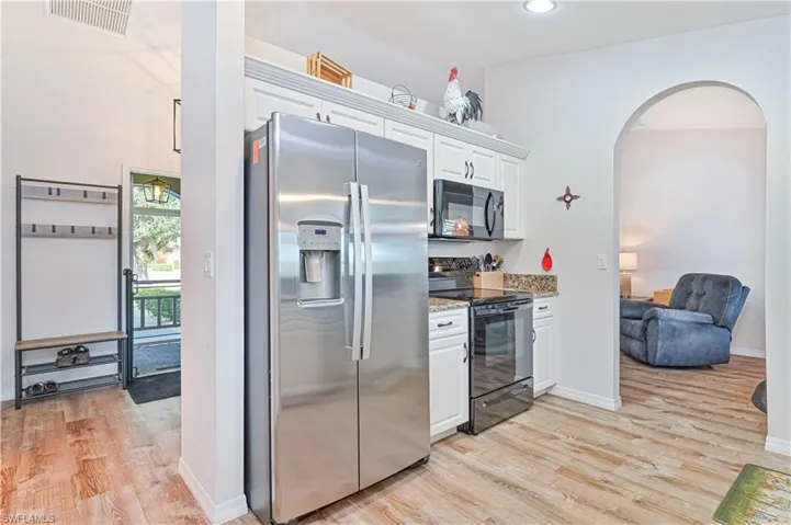 Kitchen with black appliances, white cabinets, arched walkways, light stone countertops, and recessed lighting