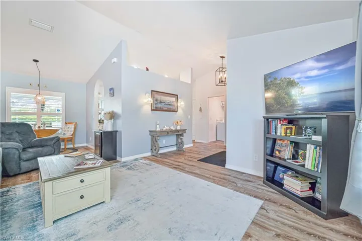 Living area with a chandelier, light wood finished floors, arched walkways, and high vaulted ceiling