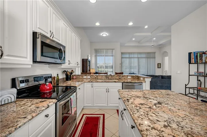 Kitchen featuring arched walkways, light tile patterned flooring, stainless steel appliances, a sink, and white cabinetry