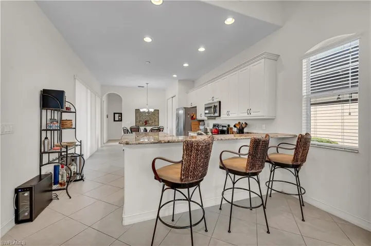 Kitchen with arched walkways, light stone counters, stainless steel appliances, a peninsula, and white cabinetry