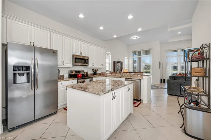 Kitchen with light tile patterned floors, a peninsula, white cabinetry, appliances with stainless steel finishes, and a center island