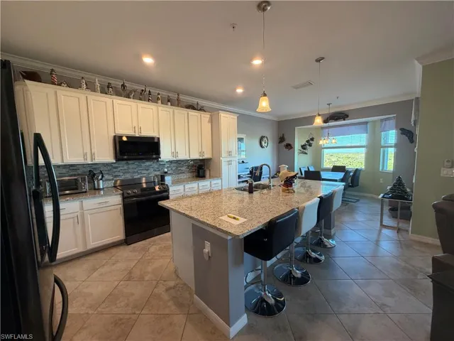 Kitchen featuring black appliances, light stone countertops, an island with sink, decorative backsplash, and white cabinets