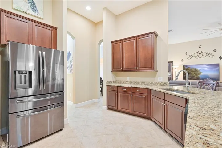 Kitchen with stainless steel fridge, light stone countertops, arched walkways, light tile patterned floors, and ceiling fan