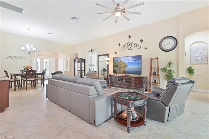 Living area featuring arched walkways, a chandelier, light tile patterned floors, and a ceiling fan
