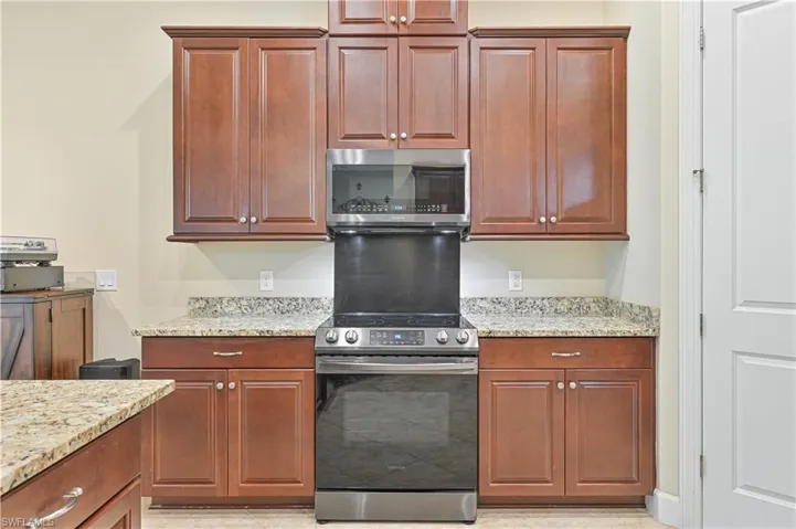 Kitchen with stainless steel appliances, light stone counters, and brown cabinets