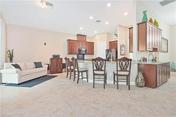 Kitchen featuring open floor plan, a kitchen bar, light tile patterned flooring, light stone countertops, and recessed lighting