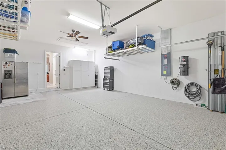 Garage featuring stainless steel fridge with ice dispenser, ceiling fan, electric panel, and a garage door opener