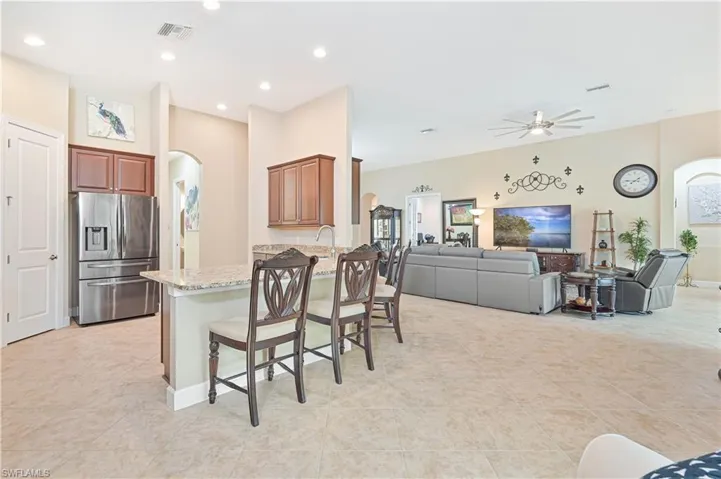 Kitchen with arched walkways, a kitchen bar, stainless steel fridge, open floor plan, and light stone countertops
