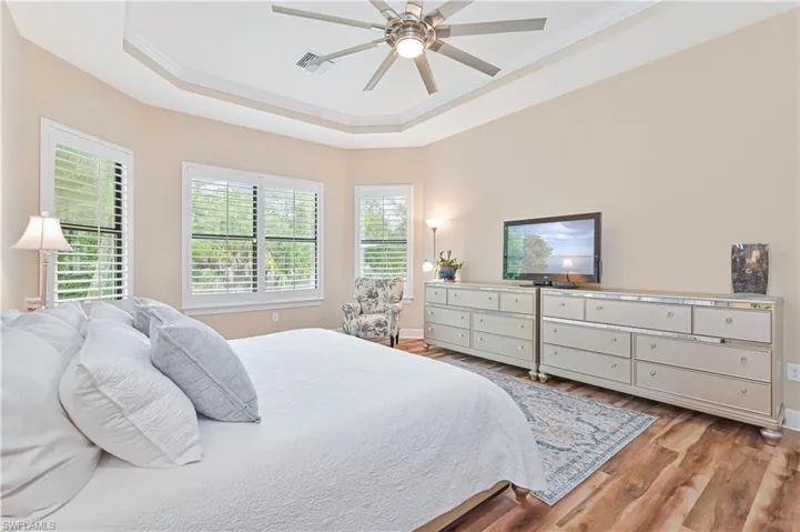 Bedroom with a raised ceiling, light wood finished floors, ceiling fan, and crown molding